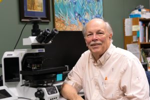 Ernest Bernard sitting in his lab beside a microscope. 